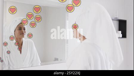 Bild von Mediensymbolen über birassischer Frau, die im Badezimmer lächelt Stockfoto
