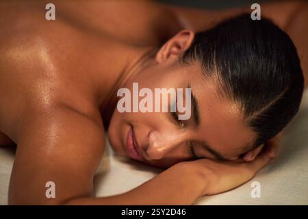 Frau, die sich während einer Spa-Massage auf einem weichen Tisch mit ruhigem Ausdruck und ruhiger Atmosphäre erholt, während sie professionell massiert wird Stockfoto