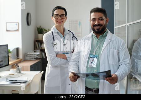 Zwei lächelnde Mediziner-Mann-Frau, die Labormäntel mit überkreuzten Armen in der Klinik trägt Stockfoto