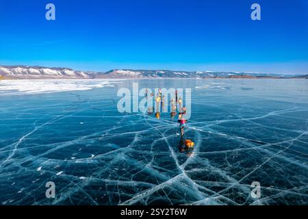 Blick von oben zum Touristenspaziergang auf glattem Untergrund. Menschen mit Schlitten bewegen sich auf dem blauen, klaren Eis. Überquerung des Baikalsees im Winter. Risse glänzend Stockfoto