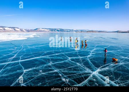Blick von oben zum Touristenspaziergang auf glattem Untergrund. Menschen mit Schlitten bewegen sich auf dem blauen, klaren Eis. Überquerung des Baikalsees im Winter. Risse glänzend Stockfoto