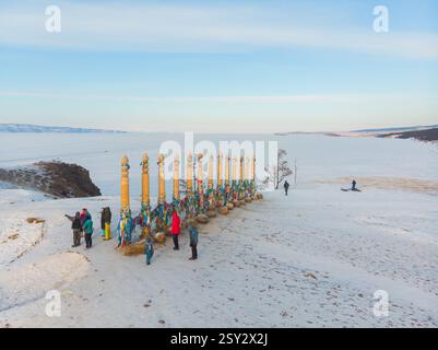 Blick von oben auf das berühmte Cape Burhan. Touristen binden bunte Bänder an hölzernen Ritualstangen und machen Wünsche. Gefrorener Baikalsee. Schamanenstein und klein Stockfoto