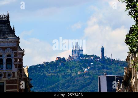 Blick auf den Berg Tibidabo in Barcelona, Spanien, mit der Kirche Sagrat Cor, dem Vergnügungspark Tibidabo und dem Torre de Collserola unter teilweise bewölktem Himmel Stockfoto