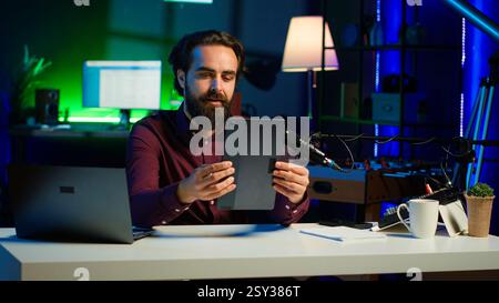 Ein technischer Experte präsentiert ein Tablet im Einstiegssegment mit niedrigen Budgets für interessierte Zuschauer und filmt im Studio. Viraler Content-Ersteller, der digitale Geräte vor dem Internet-Publikum überprüft, Kamera A Stockfoto