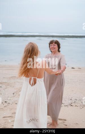 Eine junge Frau und ihre ältere Mutter drehen sich und halten Hände am Strand Stockfoto