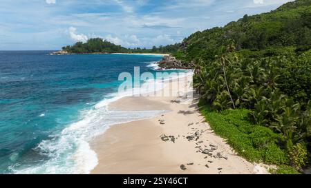 Weißer Sandstrand mit türkisfarbenen Wellen und üppigem Grün im Hintergrund. Anse Boileau. Seychellen, Mahe. Stockfoto