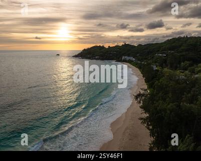 Die Sonne untergeht über einer ruhigen Küste mit sanften Wellen, die sich in goldenen Tönen spiegeln. Anse Intendance. Seychellen, Mahe. Stockfoto