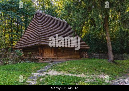 Ein charmantes Holzhaus mit einem Strohdach steht umgeben von üppigem Grün. Goldene Sonnenstrahlen filtern durch die Bäume und schaffen eine Ruhe Stockfoto