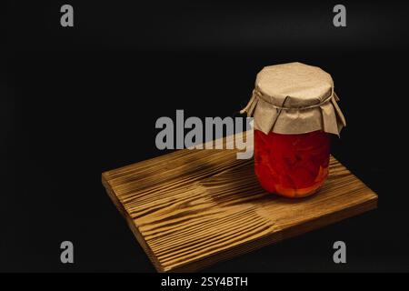Auf einem Holzbrett befindet sich ein Glas mit hausgemachten Konserven. Das Glas enthält eingelegte süße Paprika, Tomaten und gesalzenes Schmalz, was die Tradition unterstreicht Stockfoto