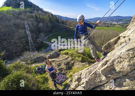 Zwei weibliche Klettererinnen klettern auf einer Klippe, einer steigt an, während der andere sicherstellt, um Teamwork und Abenteuer in einer natürlichen Umgebung zu zeigen Stockfoto