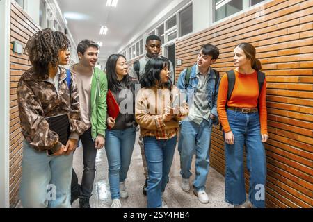 Eine Gruppe verschiedener Universitätsstudenten läuft den Schulflur entlang, diskutiert und arbeitet auf dem Weg zur Klasse zusammen Stockfoto