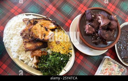 Traditionelles brasilianisches Mittagessen mit gegrilltem Schweinefleisch, Feijoada, Reis, Farofa und Kohlgemüse, serviert auf einer karierten Tischdecke Stockfoto