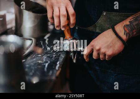 Der Barista tönt Kaffeesatz mit einem Portafilter auf einer Marmortheke Stockfoto