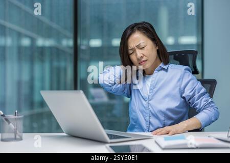 Müde und überarbeitete Frau im Büro, Geschäftsfrau leidet unter Nacken- und Rückenschmerzen. Lange monotone sitzende Arbeit am Computer. Stockfoto