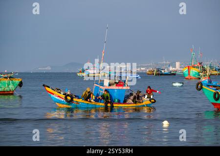 Fischer auf einem Fischerboot fahren vor dem Strand von Mui ne, Mũi Né, viele Fischerboote in der Ferne. Stockfoto