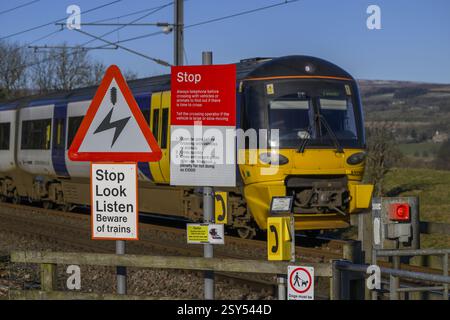 Northern Rail Zug fährt über unbemannte Bahnübergänge (streckenseitige Eisenbahnwarnungen) - Burley in Wharfedale, West Yorkshire, England, Großbritannien. Stockfoto