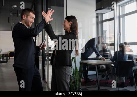 Geschäftsleute feiern Erfolg mit High-Five in einem modernen Büro. Konzept von Teamarbeit, Leistung, Zusammenarbeit und Unternehmenskultur Stockfoto