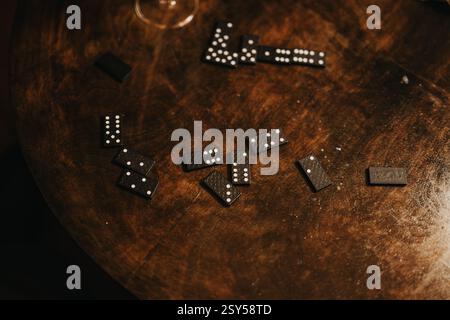 Verstreute schwarze Domino-Fliesen auf einem Holztisch in warmer Beleuchtung Stockfoto