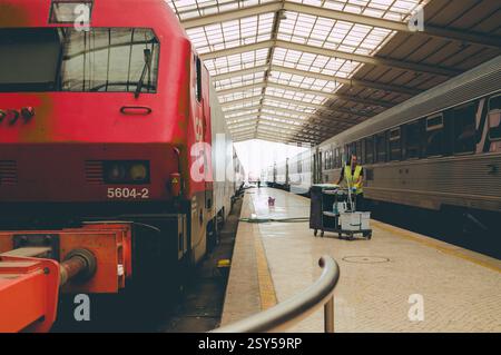 Ein Arbeiter in einer reflektierenden Weste schiebt einen Reinigungswagen entlang der Plattform am Bahnhof Santa Apolónia Stockfoto