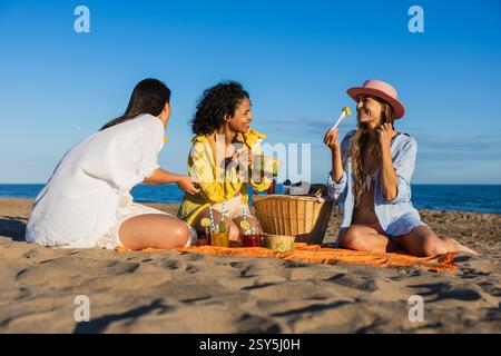 Multiethnische Freundinnen genießen ein Picknick am Strand Stockfoto