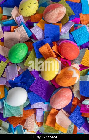 Blick von oben auf hell dekorierte Ostereier auf einem mehrfarbigen Krepppapierhintergrund mit festlicher und fröhlicher Atmosphäre. Stockfoto