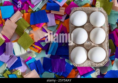 Blick von oben auf weiße Eier in einem Karton auf einem farbenfrohen Papierhintergrund. Stockfoto