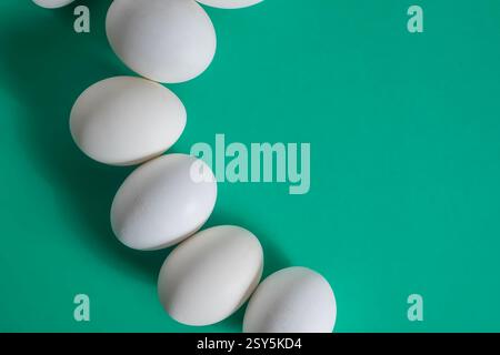 Weiße Eier sind kunstvoll auf einer sauberen grünen Oberfläche angeordnet und verfügen über einen Kopierraum für Text. Stockfoto