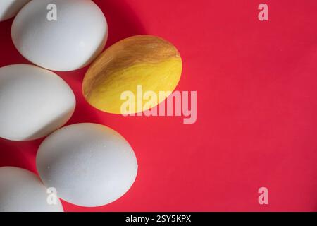 Ein gelbes Ei hebt sich unter weißen Eiern auf rotem Hintergrund für eine Ostergrußkarte hervor. Stockfoto