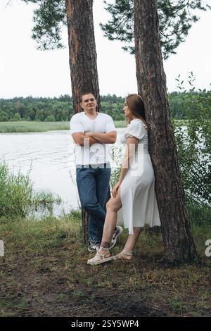 Romantisches Paar, das sich an einem bewölkten Tag in der Nähe eines Sees und eines Waldes küsst und umgibt. Stockfoto