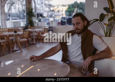 In einem modernen Café sitzt ein lässig gekleideter Mann an einem Marmortisch. Die warme Beleuchtung und das stilvolle Dekor sorgen für eine entspannte Atmosphäre in der späten Nacht Stockfoto