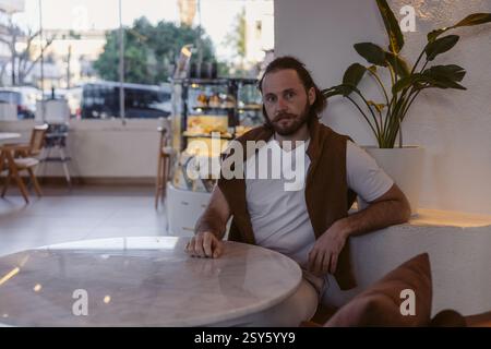 In einem modernen Café sitzt ein lässig gekleideter Mann an einem Marmortisch. Die warme Beleuchtung und das stilvolle Dekor sorgen für eine entspannte Atmosphäre in der späten Nacht Stockfoto
