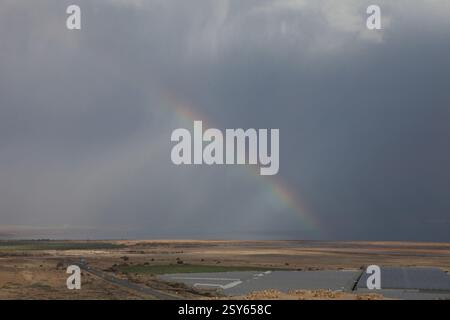Regenbogen und ein Lichtspiel am bewölkten Himmel an einem regnerischen Tag über dem Toten Meer, dem See, dem Wasser, der Küste und der Landwirtschaft Stockfoto