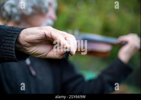 Eine Nahaufnahme einer Geigerhand, die den Bogen hält, mit einem verschwommenen Hintergrund, der einen älteren Musiker zeigt, der im Freien Geige spielt. Stockfoto