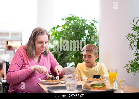 Großmutter im Rollstuhl und Enkel essen zusammen in einem Restaurant in einem Einkaufszentrum Stockfoto