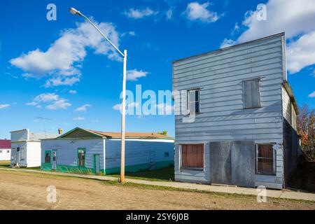Ein kleines Haus mit einem grünen Dach liegt an einer Straße. Im Hintergrund befindet sich ein großes Gebäude mit einem weißen Dach Stockfoto