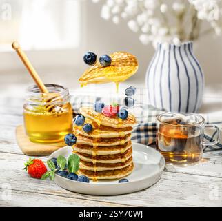 Köstliche Pfannkuchen werden mit goldenem Honig getränkt und wunderschön mit frischen Heidelbeeren und Erdbeeren für ein romantisches Frühstück geschmückt Stockfoto