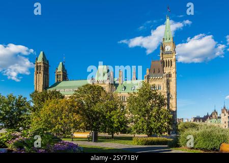 Großes Gebäude mit Uhrenturm und grünem Dach. Das Gebäude ist von Bäumen und einer Bank umgeben Stockfoto