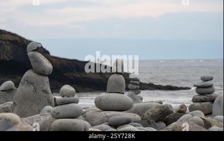 Säulen aus Zen-Kieselsteinen, die Steine balancieren auf einem Kieselstrand. Im Hintergrund sind Klippen und die Einzelfigur eines Fischers Stockfoto