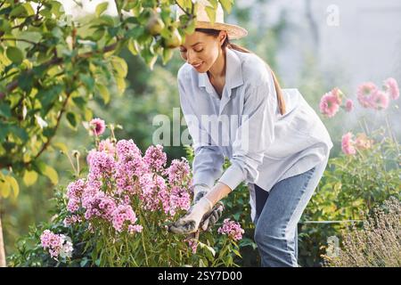 Blumenpflege. Die junge, fröhliche Frau ist tagsüber im Garten. Stockfoto