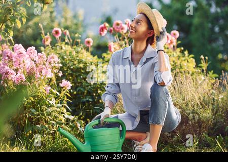 Vorbereitung für das Gießen der Blumen. Die junge, fröhliche Frau ist tagsüber im Garten. Stockfoto