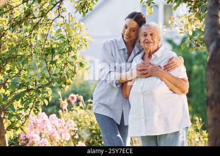 Umarmen und lächeln. Die junge Frau ist bei ihrer älteren Mutter im Garten. Stockfoto