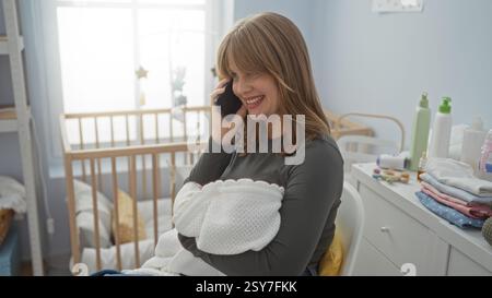 Frau plaudert am Telefon in einem gemütlichen Kinderzimmer, während sie das Baby in einer Decke hält, umgeben von wichtigen Dingen und Sonnenlicht, das sanft durch das Fenster wi strömt Stockfoto