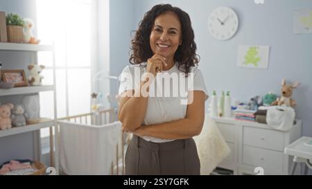 Frau, die im Schlafzimmer steht und selbstbewusst mit der Babywiege in einem wunderschön eingerichteten Zimmer lächelt und durch ihre PR ein Gefühl von Wärme und Familienbetreuung weckt Stockfoto