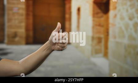 Ein Mann zeigt die Daumen mit der Hand in einer Straßenlandschaft im Freien, betont Positivität und Anerkennung in einer städtischen Umgebung, mit einer verschwommenen Geschichte Stockfoto
