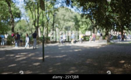Menschen gehen in einem verschwommenen Bild der Villa borghese Gärten in rom mit Bäumen und Sonnenlicht, die draußen einen defokussierten und Bokeh-Effekt erzeugen. Stockfoto