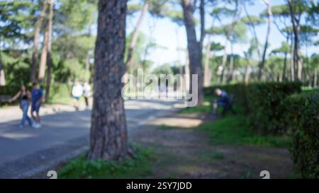 Outdoor-Szene mit verschwommenen Menschen, die durch die Gärten der Villa borghese mit defokussierten Bäumen und Pfad in rom spazieren. Stockfoto