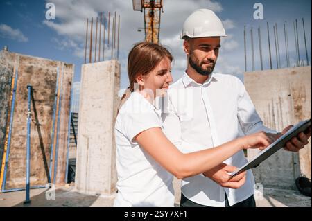 Lesen des Dokuments in Notepad. Mann in Uniform, der mit Frau auf der Baustelle arbeitet. Stockfoto