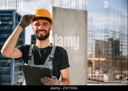 Posieren für eine Kamera, mit Notizblock. Wunderschönes Porträt. Mann in Uniform arbeitet auf der Baustelle. Stockfoto
