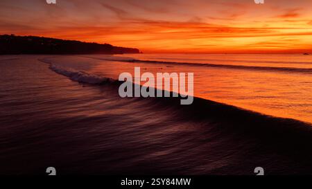 Fantastischer warmer Sonnenuntergang und Ozean mit Silhouette der perfekten Surfwelle auf Bali. Stockfoto
