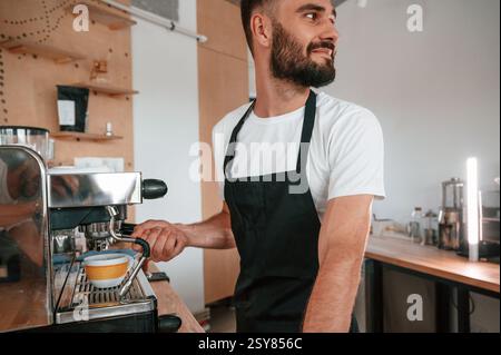 Verwenden der Kaffeemaschine. Cafe-Mitarbeiter in weißem Hemd und schwarzer Schürze ist drinnen. Stockfoto